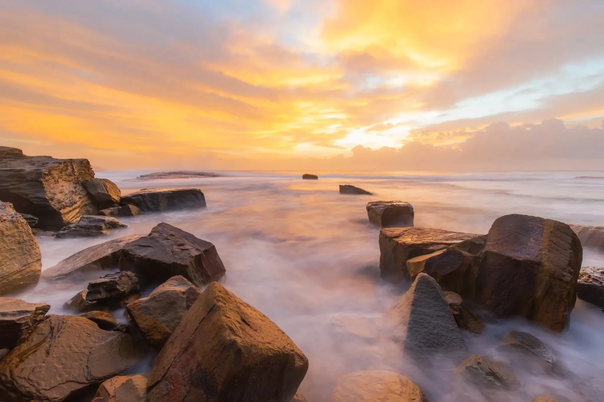 Golden sunrise over ocean rocks on the Central Coast, waves flowing gently